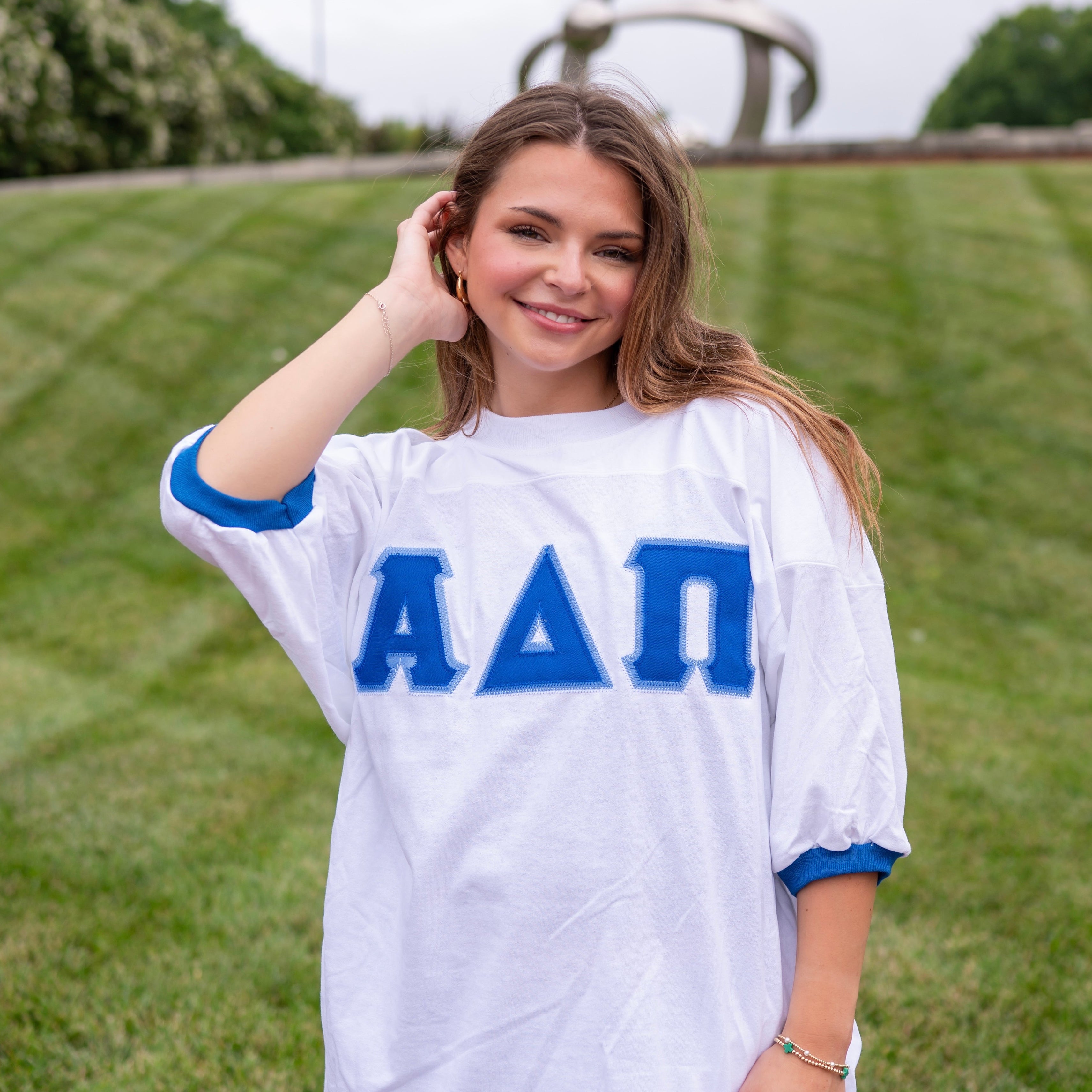 Woman wearing a white oversized shirt with blue Alpha Delta Pi Greek letters on a grassy field